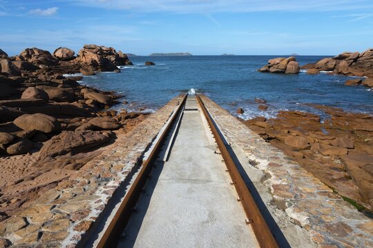 A stone path leads through a rocky coastal landscape to the blue sea under a clear sky, Cale de Porz-Kamor, Porz-Kamor slipway for lifeboats, Ploumanac'h, Ploumanach, Perros-Guirec, C&ocirc;tes-d'Armor, Brittany, France