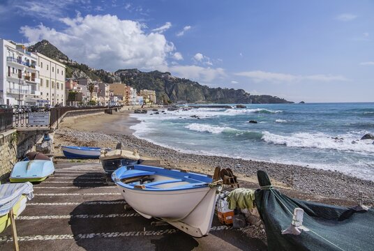 Fishing boats on the beach with sea surf in front of the promenade, Giardini-Naxos, east coast, Sicily, Italy