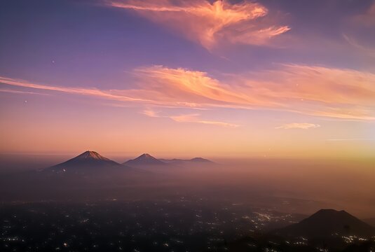 Beautiful twilight landscape featuring Mount Merbabu with distant views of Mount Sindoro and Mount Sumbing in Central Java, Indonesia. The scene showcases vibrant pink and purple clouds, atmospheric m