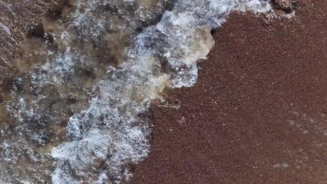 Il bagnasciuga della spiaggia col mare calmo e cristallino.
Vista dall'alto delle onde sulla sabbia della spiaggia. Ripresa in 4K
