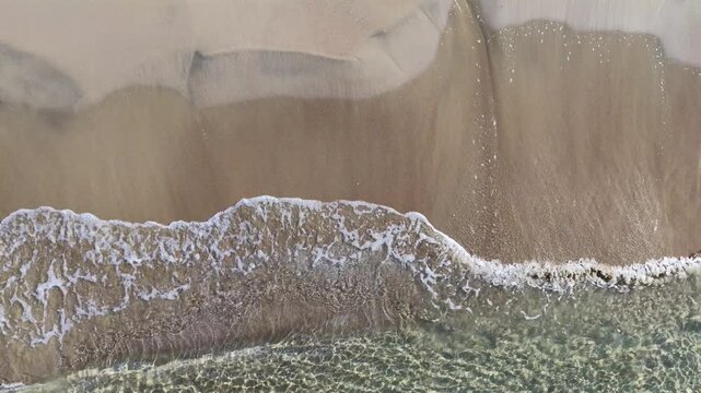 Il bagnasciuga della spiaggia col mare calmo e cristallino.
Vista dall'alto delle onde sulla sabbia della spiaggia. Ripresa in 4K
