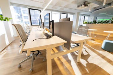 Modern office workspace featuring multiple desks with computer monitors, ergonomic chairs, and...