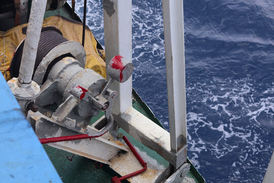 a maritime winch mechanism and cable system mounted on a ship deck with open ocean water in the background