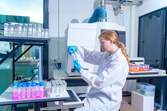 Scientist in laboratory coat and gloves examines a test tube with scientific equipment