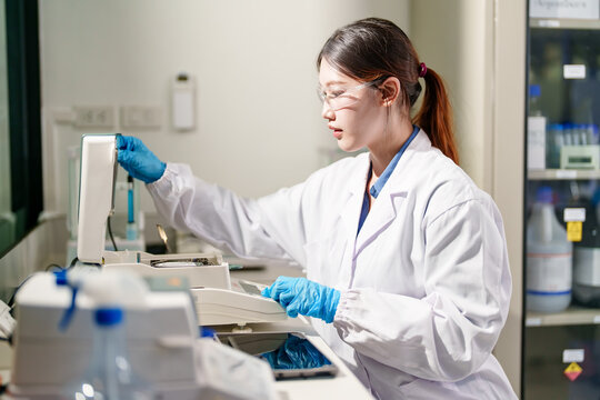 Young female scientist in lab coat and gloves conducting experiment with laboratory equipment