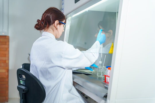 Scientist in protective gear working with samples inside a sterile laboratory fume hood