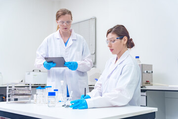 Fototapeta premium Two female scientists in a laboratory setting working with equipment and digital tablet