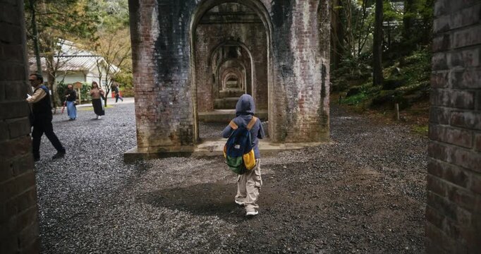 Slow motion shot following little boy walking under brick arches under old Japanese bridge