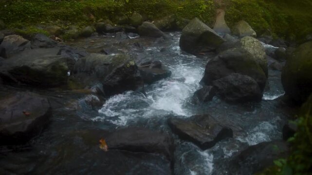 Mountain stream flows rapidly between dark rocks in a lush forest on the island of Java, Indonesia creating a peaceful natural environment for a remote wilderness setting