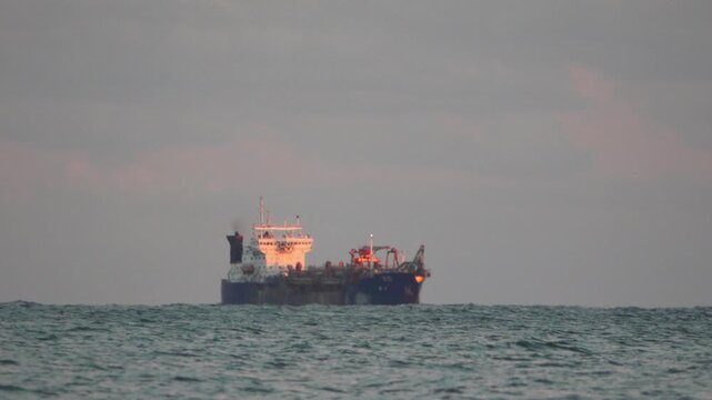 Ship ocean dredging industrial vessel silhouette at calm dark sunset twilight over rough water