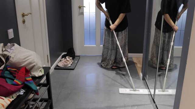 A teenager moves a flat mop across gray entryway tile near a shoe tray and mirrored closet.