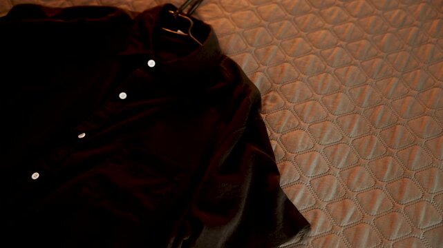 Black collared shirt with white buttons resting on a textured bedroom bedspread