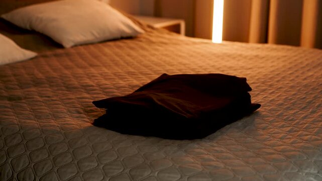 Folded dark clothing rests on a soft bed in a cozy bedroom during evening