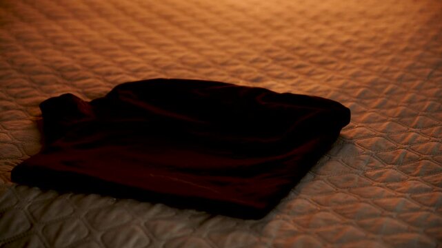 Dark shirt resting on a beige quilted bedspread under warm evening light