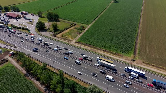 Highway Traffic Jam: An aerial view captures a bustling highway choked with a significant traffic jam, highlighting the congestion amidst agricultural fields under a bright sun.