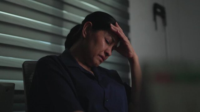 woman's despair: A woman holds her head in despair, her face etched with sadness and worry, sitting alone in a dimly lit room, conveying a sense of isolation and helplessness.