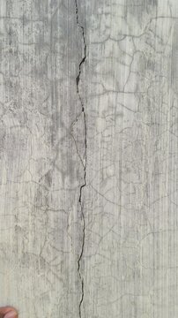 Crack or fracture visible vertical line damage in brick and cement wall surface. Structural Engineer hand check cracked gaps on building structure for safety repair and maintenance work evaluation.