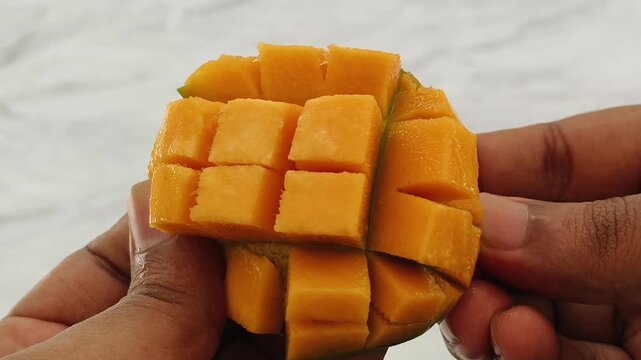 Mango fruit sweet juicy yellow ripe flesh sliced and cut into cube piece. Closeup topview of Indian adult person hand holding delicious and yummy fresh mango slice for eating. Healthy diet concept.