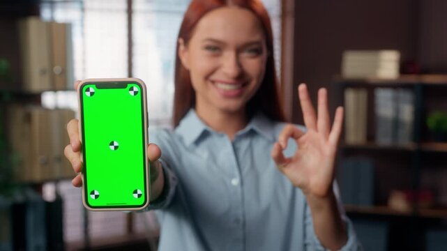 Positive smiling Caucasian business woman showing okay fine gesture with chroma key mobile phone online notification businesswoman female girl user show ok sign with smartphone green screen in office