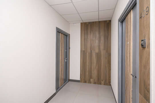 A modern hallway with light grey tiled floor, white walls, and dark grey doors with wood panels; features a wooden accent wall