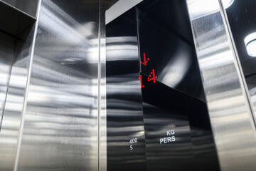 close-up of a modern elevator interior with brushed stainless steel walls  red LED display shows floor 14 with downward arrow  capacity labels «400 KG / 5 PERS» visible © evgeniykleymenov