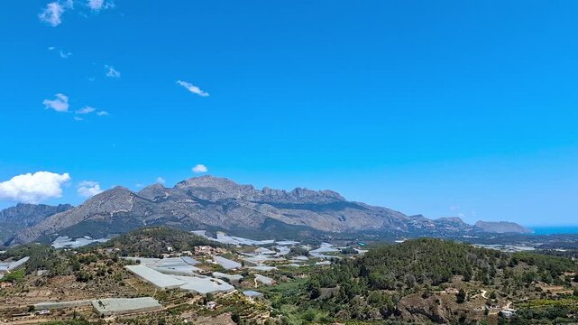 Panoramic scenic view of Polop surroundings with loquat orchards greenhouses under serrella mountain range, Mediterranean sea on the horizon, Spain.
