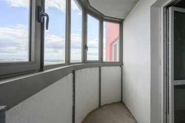 Obraz premium curved balcony with grey-framed panoramic windows, white insulated walls, and a bare concrete floor, offering a view of the sky and neighboring buildings