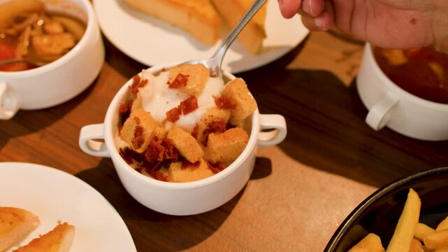 Person Eating Creamy Soup with Croutons and Bacon at Restaurant Buffet