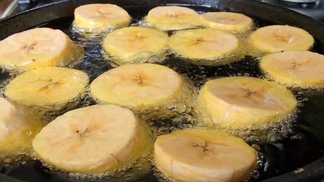 Close up of plantains being deep-fried on black cast iron pan, making patacones