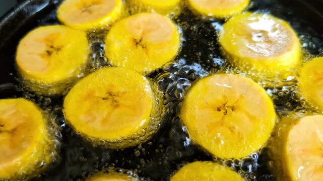Close up of plantains being deep-fried on black cast iron pan, making patacones