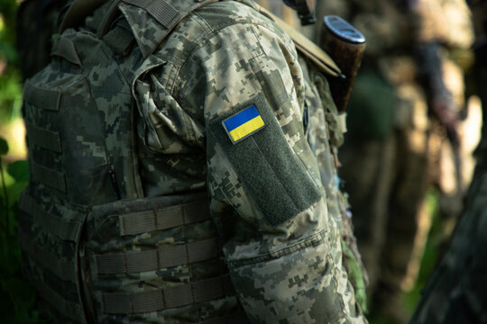 Ukrainian soldier in pixel camouflage uniform with national flag patch sitting in grass