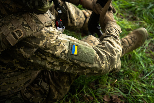 Ukrainian soldier in pixel camouflage uniform with national flag patch sitting in grass