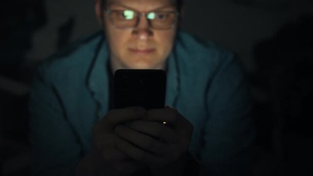 At night, bespectacled man gazes at his glowing smartphone, a vivid illustration of phone addiction-a bad habit that hijacks his focus, disrupts sleep, and mirrors modern over-use of digital devices