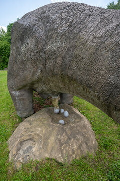 Adult dinosaur figurine laying eggs into a nest in the grass.