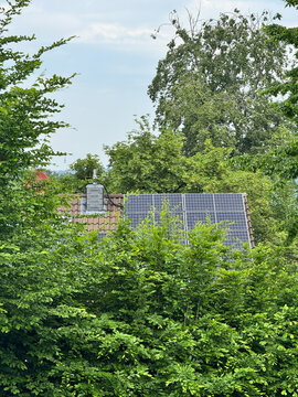 Rooftop solar panels integrated into a residential home surrounded by lush green trees