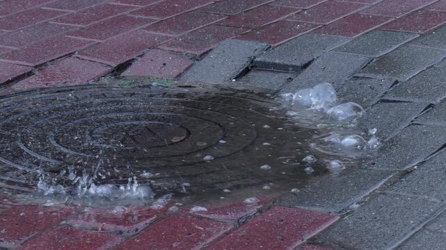 Heavy rain splashing in a puddle on a manhole cover