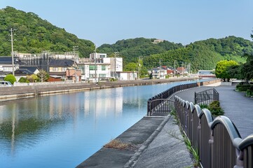 Fototapeta premium 米子市新加茂川沿いの遊歩道から見渡す愛宕山と水辺の街並み/View of Mount Atago and the Waterfront Cityscape from the Promenade Along the Shin-Kamo River in Yonago City