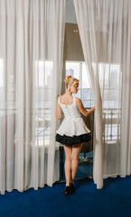 Obraz premium A girl looks out the window in a white cocktail dress.