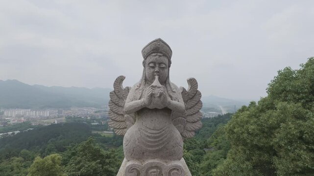 4K resolution close up shot of a stone Kalavinka statue playing a musical instrument, positioned on a mountain top overlooking a town in the background at Donglin Temple, shot in ProRes Log format.