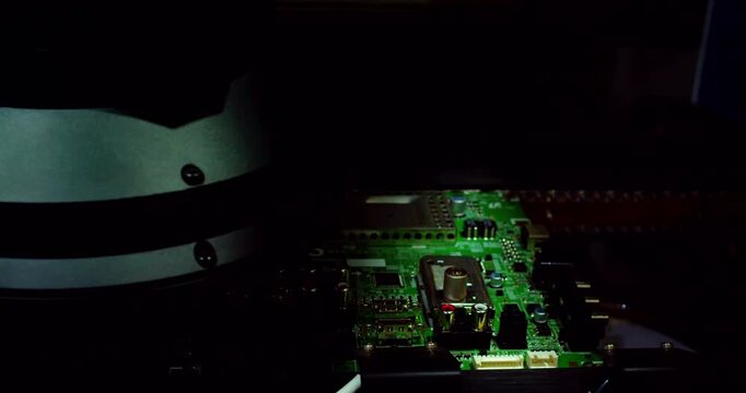 A close-up modern electronic printed circuit board  moving along an automated assembly line conveyor belt inside industrial machinery.Flashing automated optical inspection lights illuminate the board.
