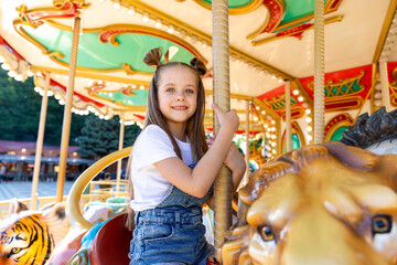 Young girl with long hair smiles while riding a lion on a colorful carousel at an amusement park during a sunny day. Happy childhood concept. Summer vacation. High quality photo © Irina Mikhailichenko
