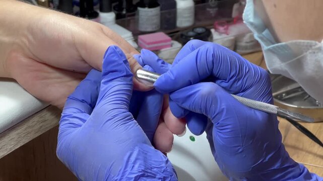 Gloved hands work carefully on a nail. Tool glides gently over nail surface. Precision and care define the process. Perfect for beauty or wellness content