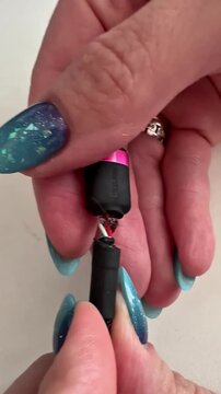 Close-up hands hold a disassembled cable. Fingers with blue glitter nails grip the exposed wires. Ring glints on one finger. Viewer sees cable's inner structure clearly