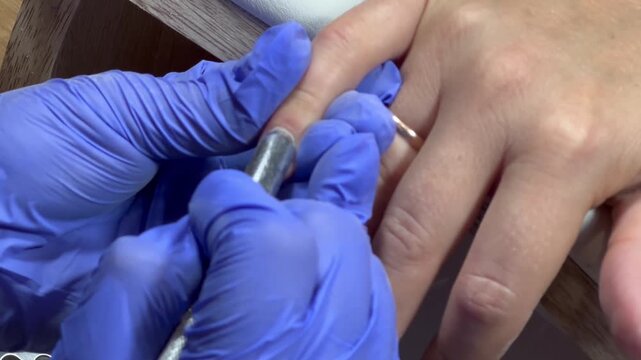 Gloved hands work carefully on a nail. Tool glides gently over nail surface. Precision and care define the process. Perfect for beauty or wellness content