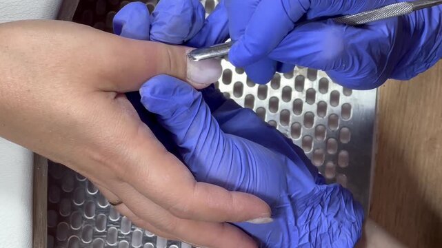 Gloved hands work carefully on a nail. Tool glides gently over nail surface. Precision and care define the process. Perfect for beauty or wellness content