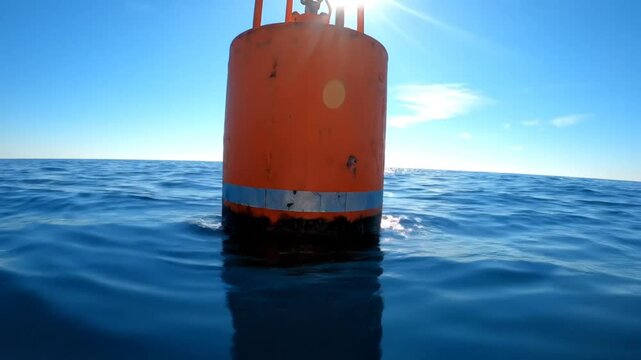 Low angle view of orange navigation buoy bobbing on clear blue ocean water under bright sunlight