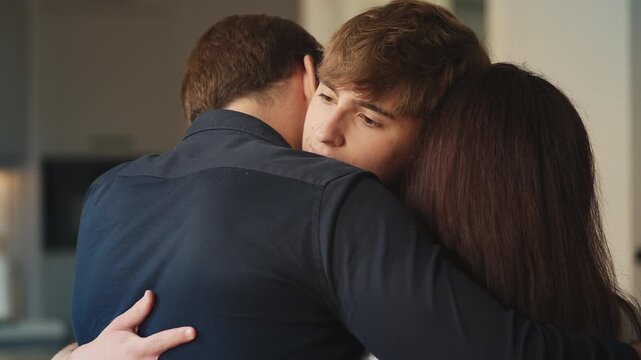Sad teenage son embracing parents before leaving home for college, farewell