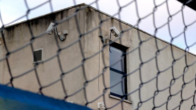 Security cameras, cctv surveillance, prison building behind chain link fence. Security system monitoring private property, industrial area or correctional facility