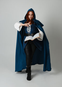 full length portrait of female model wearing medieval fantasy warrior historical costume with blue cloak. silhouette figure,  holding magical spell book on studio background.
