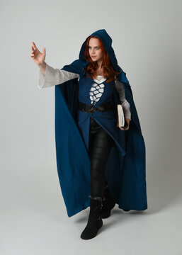 full length portrait of female model wearing medieval fantasy warrior historical costume with blue cloak. silhouette figure,  holding magical spell book on studio background.
